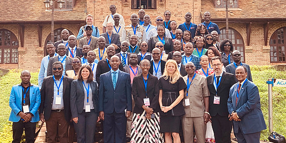Large group of conference participants poses in front of a building at Uganda Christian University.