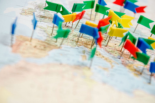 Foto: Auf einer Weltkarte sind mehrere bunte Fähnchen angeordnet.