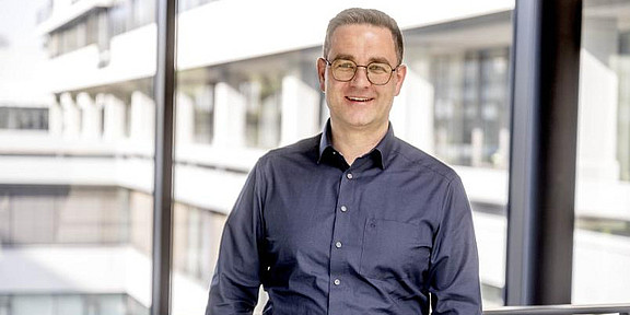 Portrait of a man in a dark blue shirt in front of a glass facade in an office building