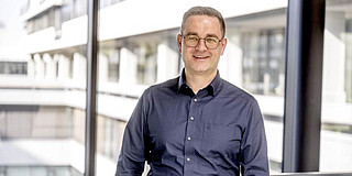 Portrait of a man in a dark blue shirt in front of a glass facade in an office building