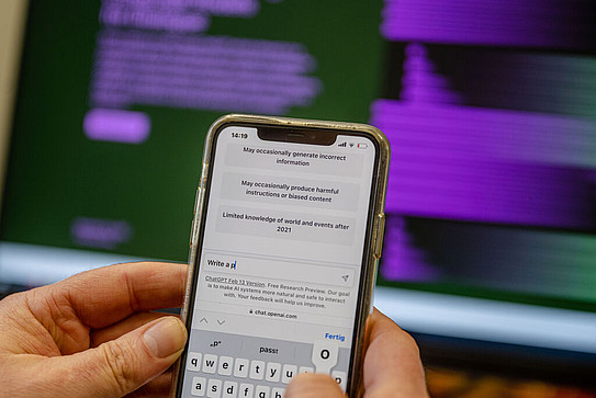 Photo: Two hands hold a smartphone and write a message to ChatGPT.